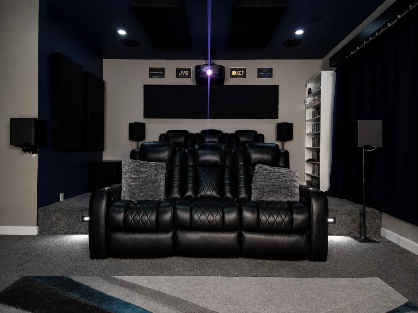 Dedicated home theater room with raised leather seating, acoustic panels, and projector
