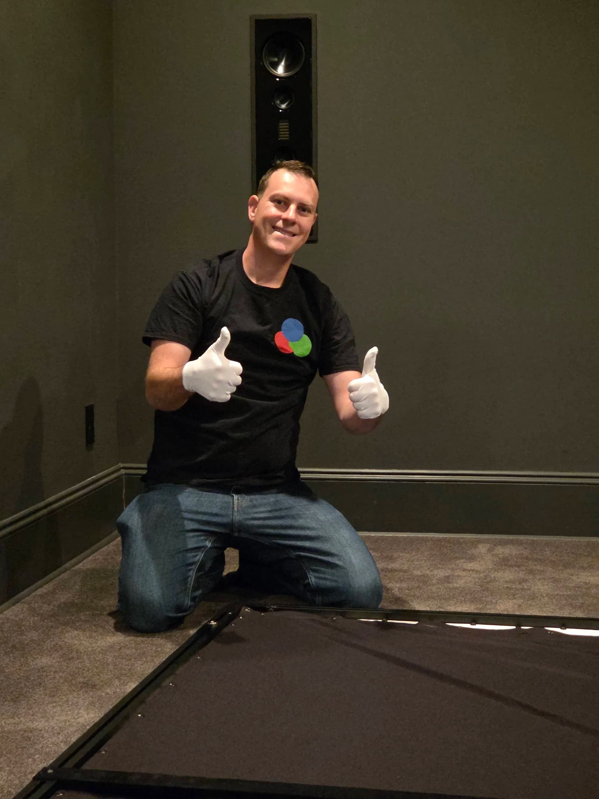 Guillaume assembling a projection screen with white gloves, Martin Logan in-wall speaker behind